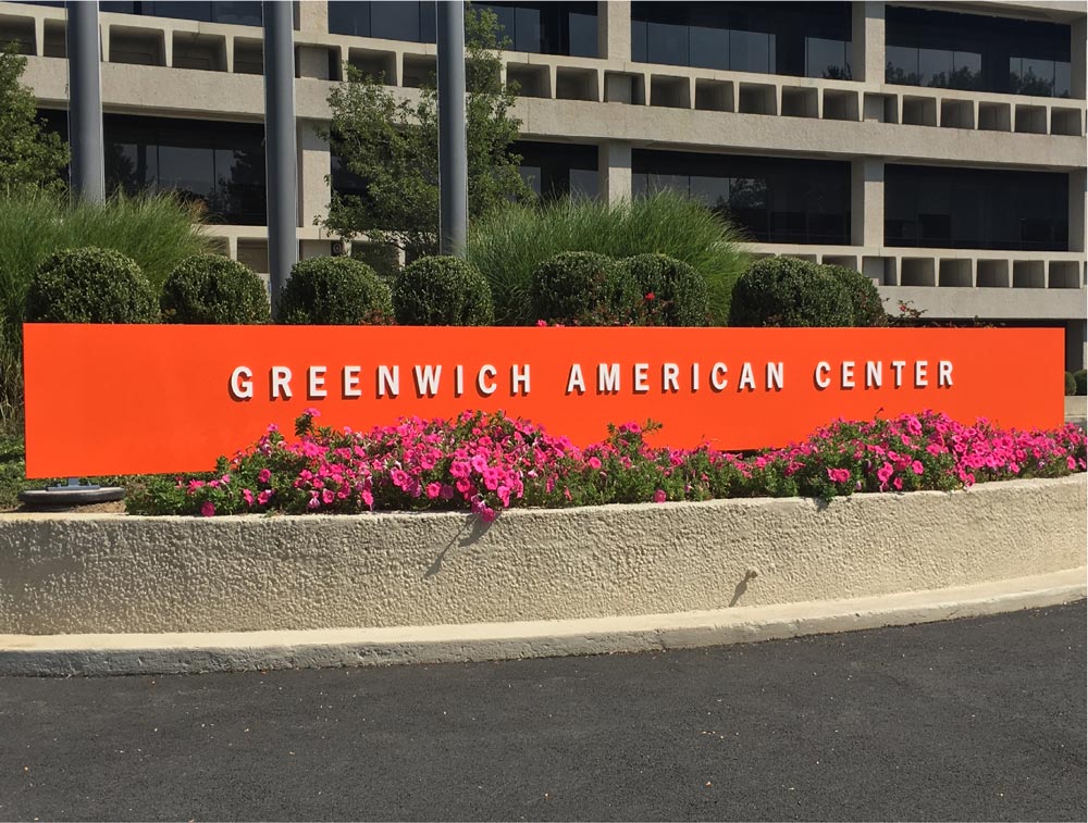 vibrant red color monument sign for Greenwich American Center, decorated with flowers