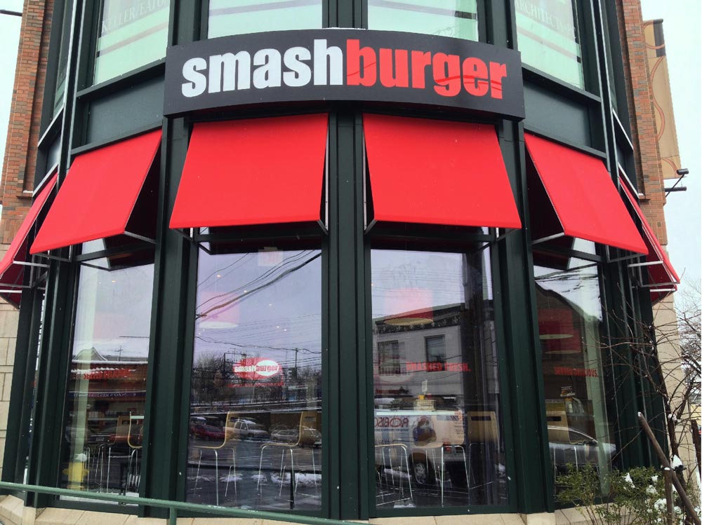 Smash Burger storefront with a curved illuminated sign cabinet and matching color awnings